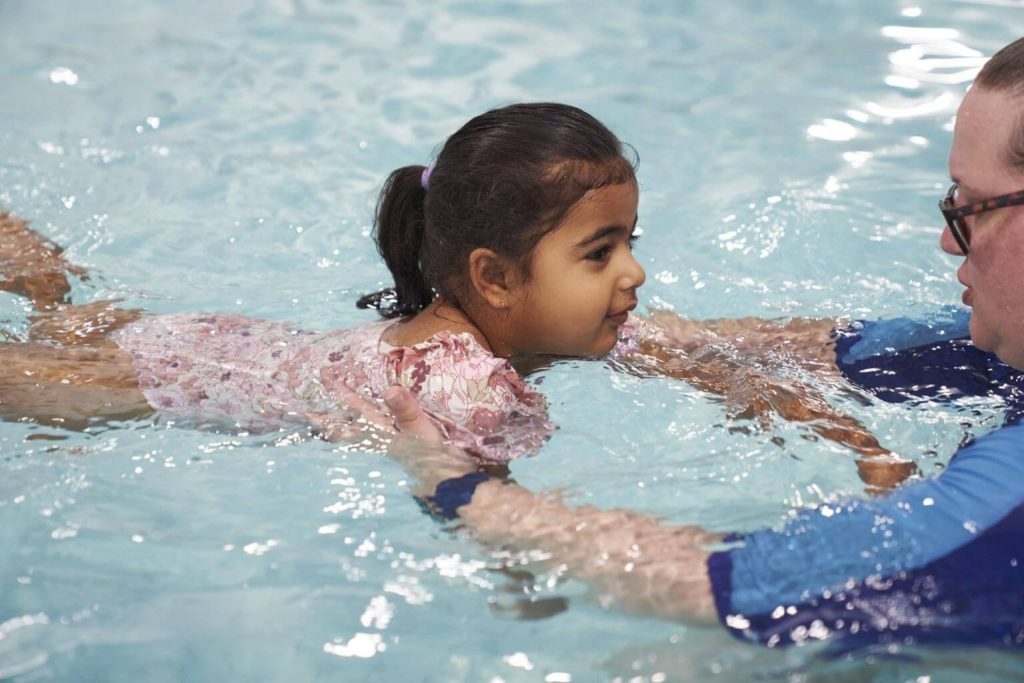 Instructor supporting a child practising swimming skills in a pool