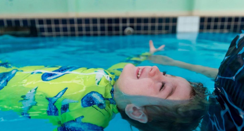 Instructor supporting a young child during a swimming lesson in a pool.