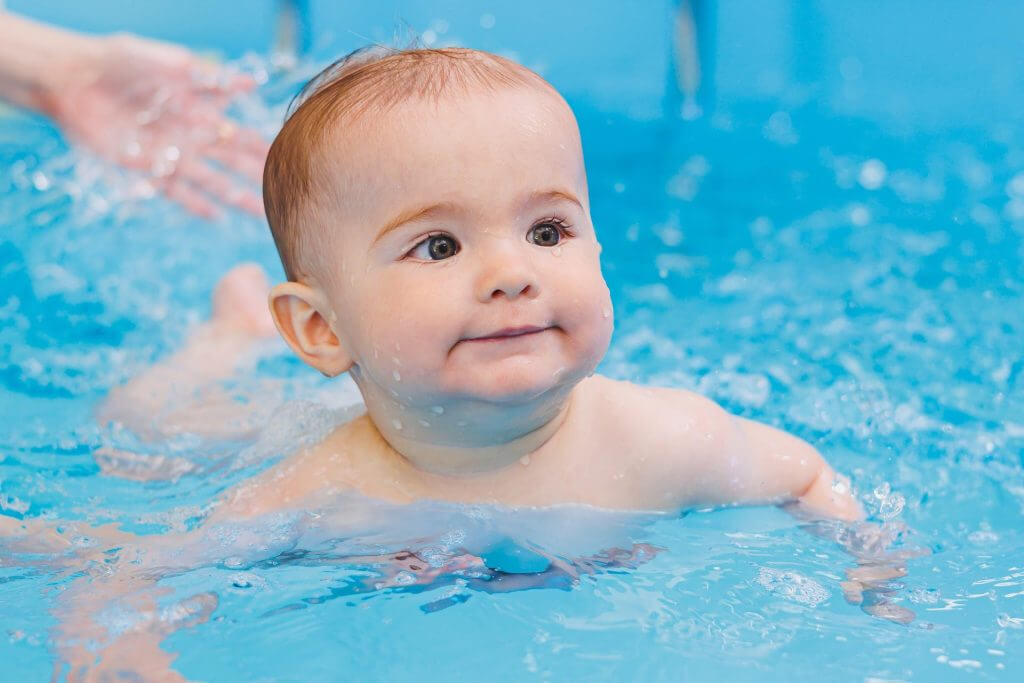 Infant participating in a baby swimming lesson in a bright indoor pool.