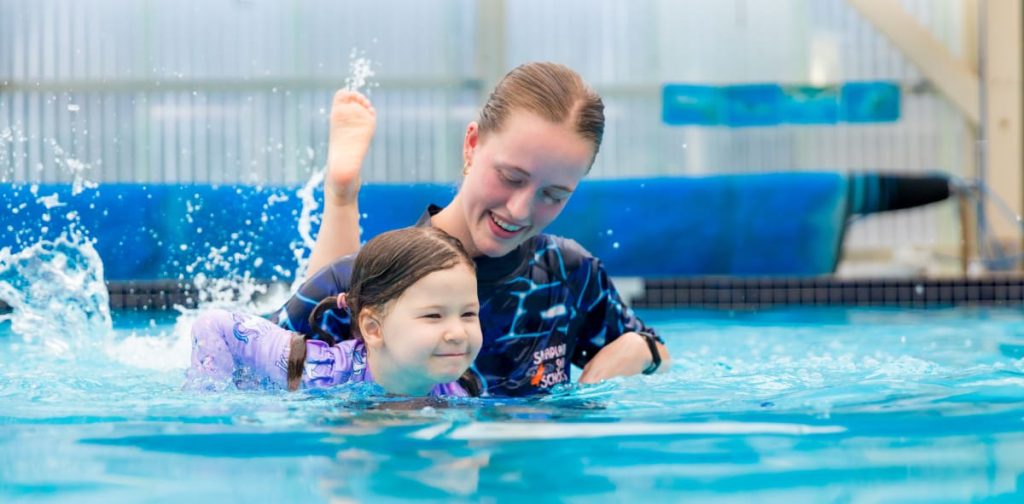 Child learning swimming skills with an instructor during a structured swimming lesson.