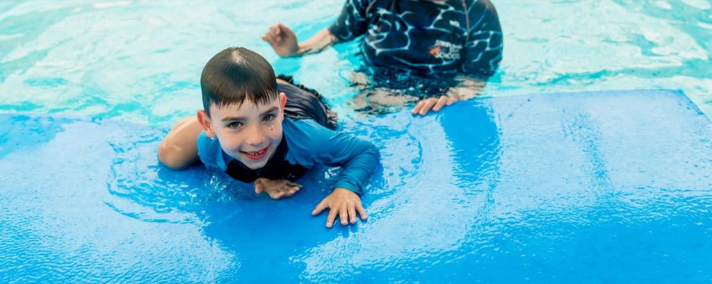 Child participating in a swimming lesson while receiving individual support from a familiar instructor.