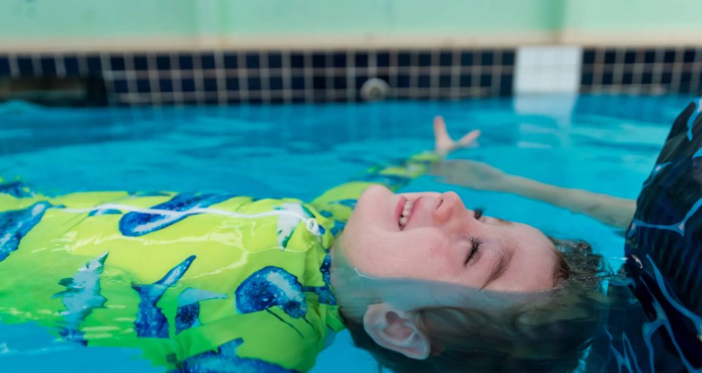 Child practising floating and body position skills during a swimming lesson with instructor support in the pool.