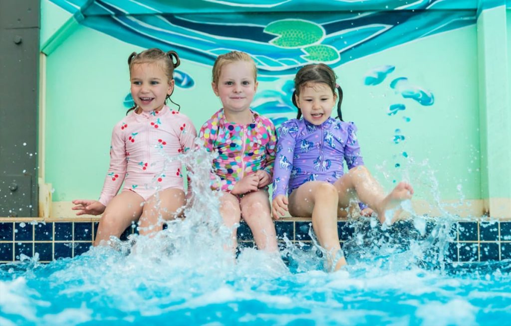 Three children participating in a small-group swimming lesson, demonstrating the personalised attention and active participation possible in smaller classes.