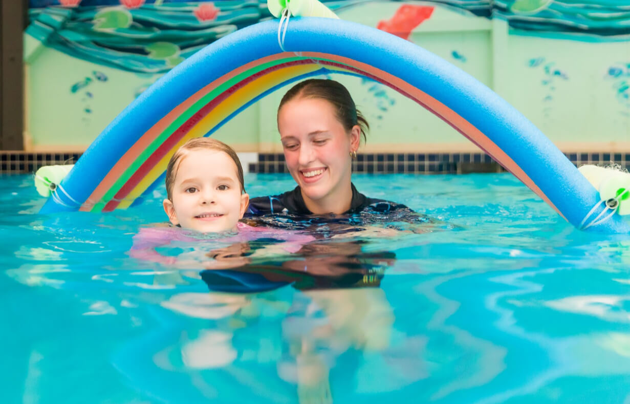 Child building water confidence with a swimming instructor during a lesson in an indoor heated pool.