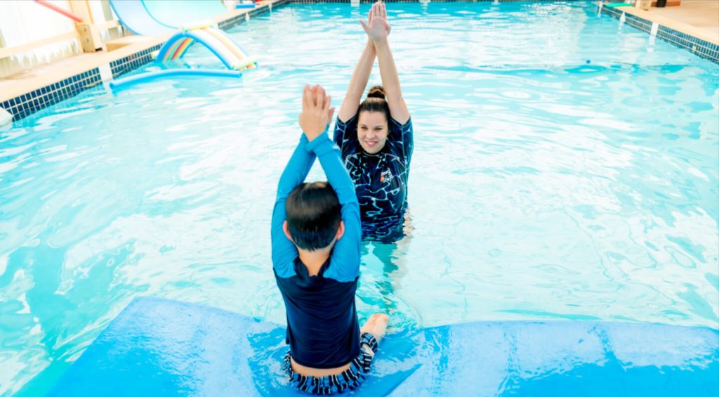 Swimming instructor guiding a child through a swimming lesson in an indoor heated pool.